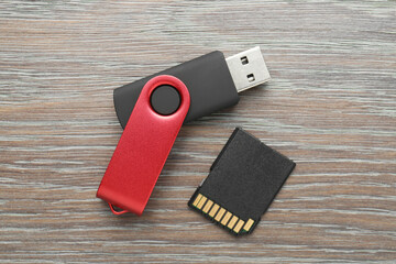 Flash drive and SD memory card on wooden background, flat lay