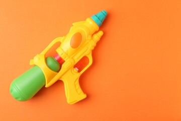 Bright plastic water gun on orange background, top view. Space for text