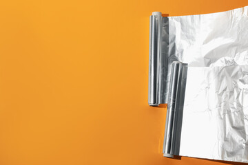 Rolls of aluminum foil on orange background, flat lay. Space for text