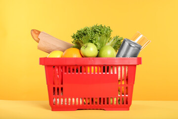 Shopping basket with different food products on yellow background