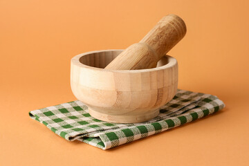 Wooden mortar, pestle and cloth on light brown background, closeup