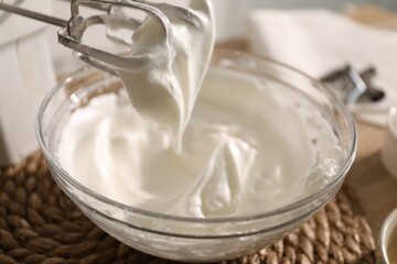 Hand mixer with whisks and bowl of whipped cream on table, closeup