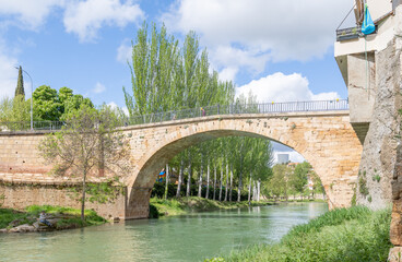 Fototapeta premium Trillo, Spain, Italy - May 05, 2025: Waterfalls running through the town of Trillo in Guadalajara, with tourists strolling around the area in Trillo, Spain.