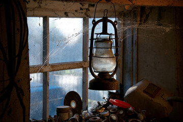 Garage in the village. Rural entourage. Bat lamp. Welder's inventory. Glimpses of light illuminate the garage tools. Vintage, kerosene lamp. Cobwebs encircle the window.