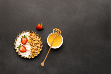 Tasty homemade dessert with cottage cheese, granola and juicy aromatic strawberries on black stone background top view. Healthy breakfast concept.