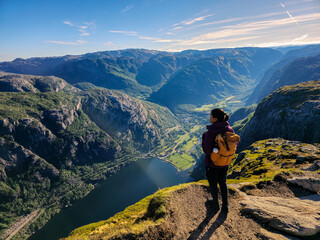 A hiker stands triumphantly at a mountain summit, gazing over the stunning fjord landscape of...