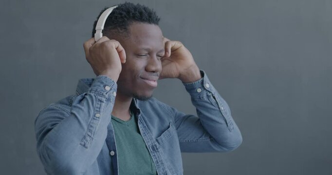 Slow motion of happy African American man listening to music with headphones enjoying song on black color background. People and modern technology concept.
