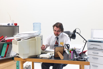 Tired office worker sitting at messy desk in office, surrounded by files, computer and paperwork,...