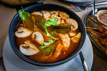 Tom Yam Khung, spicy Thai soup with shrimps and mushrooms, at a restaurant, garnished with cilantro