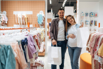 Positive facial expressions. Pregnant woman with man are in the kid's clothing store