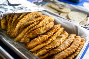 Crispy golden-brown Chebureki pastries are arranged in a metal tray lined with parchment paper at a food vendor