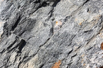 Weathered rough gray granite stone texture under sun light.