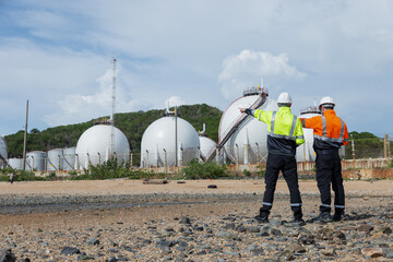 Two environmental engineers wearing safety gear observe and discuss an industrial facility with...