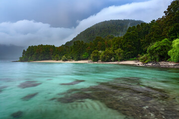 Peaceful early morning view of Lago Caburga in Chile’s Araucania Region, with mist-covered hillss, calm waters and lush green surroundings.