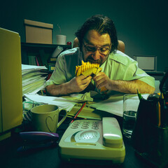 Worker eats sandwich aggressively at desk while buried in paperwork during call, showing stress,...