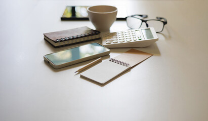office desk table with mobile, calculator and notebook with accessories for work on white table