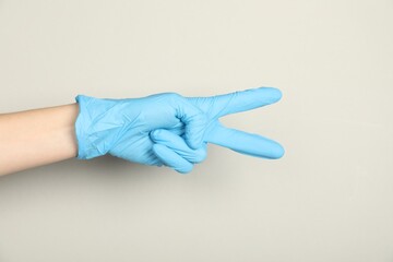 Doctor in medical glove showing two fingers on light grey background, closeup