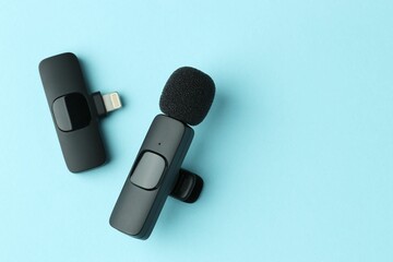 Lavalier microphone and wireless receiver on light blue background, flat lay. Space for text