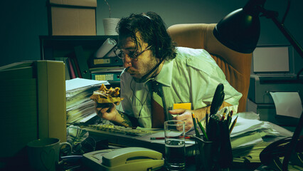 Office worker with headset eats sandwich while working at messy desk in dimly lit, green-tinted room. Burnout, lack of work-life balance. Concept of overwork, stress, and modern office demands.