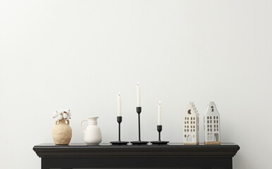 Stylish candlesticks with burning candles and other decor on fireplace near white wall indoors,...