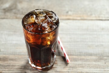 Refreshing cola with ice cubes in glass and straw on wooden table, closeup. Space for text