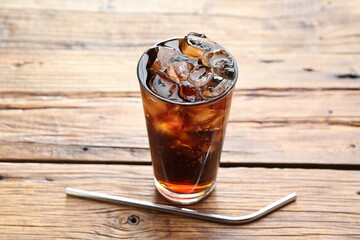 Refreshing cola with ice cubes in glass and straw on wooden table, closeup