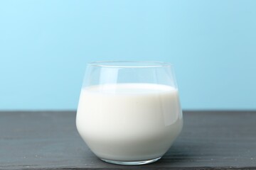 Glass of fresh milk on wooden table against light blue background
