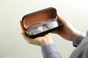 Woman holding case with stylish glasses and cleaning cloth on light background, closeup