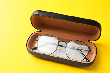 Case with stylish glasses and cleaning cloth on yellow background