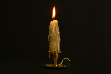 Burning candle in candlestick on black background