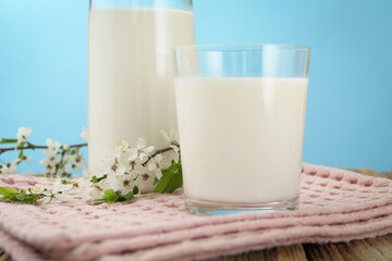 Fresh milk and blossoms on wooden table against light blue background, closeup