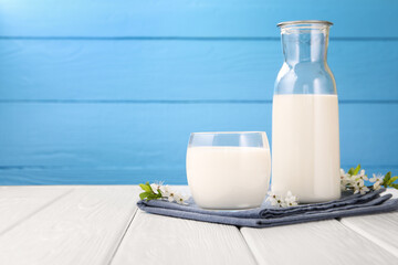 Fresh milk and blossoms on white wooden table against light blue background, closeup. Space for text