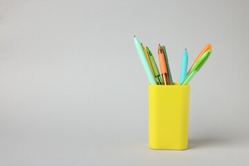 Ballpoint pens in holder on grey background. Space for text