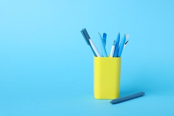 Ballpoint pens in holder on light blue background. Space for text