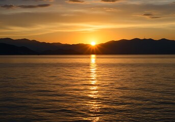 Naklejka premium A golden hour sunset over a calm body of water with silhouetted mountains in the background view