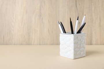 Ballpoint pens in holder on beige table against wooden background. Space for text