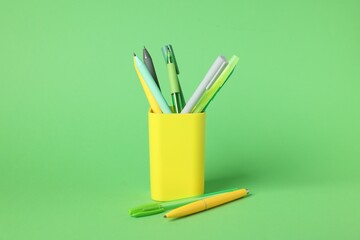 Ballpoint pens in holder on green background, closeup