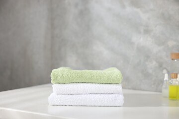 Stack of clean towels and cosmetic products on white table indoors