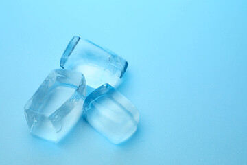 Cubes of clear ice on light blue background, closeup. Space for text