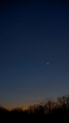 Crescent young Moon with stars, planets and countryside silhouettes.