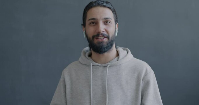 Portrait of joyful Middle Eastern man making online video call showing thumbs-up looking at camera on gray color background.