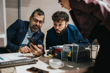 Two business people in formal attire share a surprising moment while viewing a phone. The scene suggests a thriving office atmosphere fostered by effective communication and shared interests.