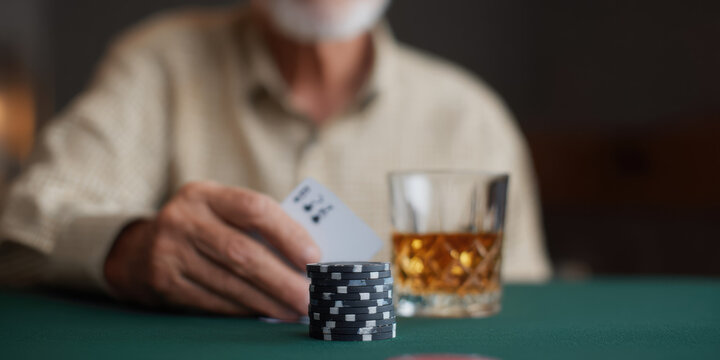 An elderly person is playing poker with chips and cards on a table, alongside a glass of whiskey. Concept: leisure, gaming, concentration, relaxation