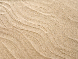 Beach sand background with natural wave pattern. Summer background of beach sand with small stones along the edges. Tourism, vacation and holidays concept. Top view.