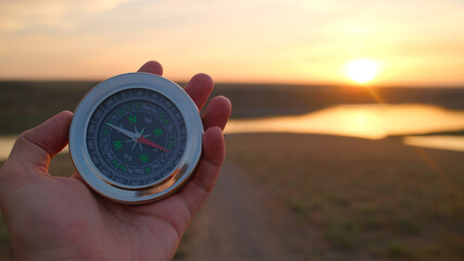 Hand holding compass during sunset over river landscape representing navigation and exploration...
