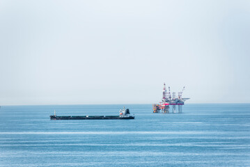 Seascape with small cargo ship and offshore oil drilling platform stands in the midst of a calm, blue sea.