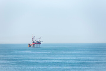 Seascape with offshore oil drilling platform that stands in the midst of a calm, blue sea.