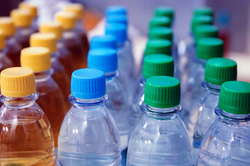 Plastic water and beverage  bottles with multicolored caps arranged in rows for packaging and consumer product display. Selective focus
