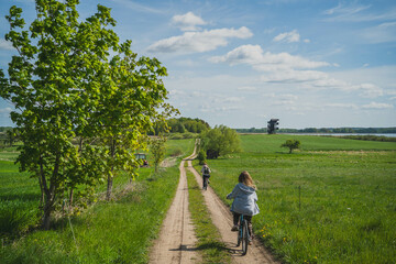 Mother and daughter, two cyclists ride through meadows, forest in Masuria. Spring, May, Poland.