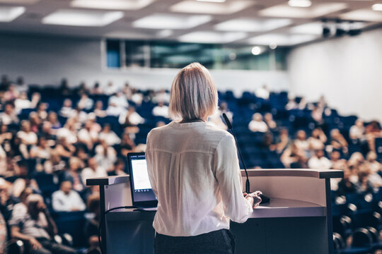 Female speaker giving a talk on corporate business conference. Unrecognizable people in audience at conference hall. Business and Entrepreneurship event